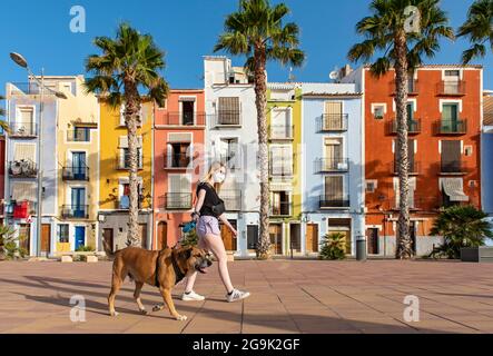 Une jeune femme marche le chien devant des maisons colorées en bord de mer, cases de couleurs, Carrer Arsenal, Villajoyosa, Espagne Banque D'Images