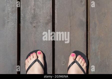 Pieds de femme en tongs sur une petite jetée ronde en bois vue d'en haut. Banque D'Images