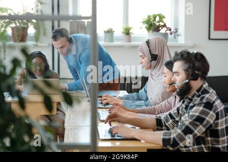 Jeunes opérateurs consultant des clients en ligne contre deux collègues discutant des données Banque D'Images