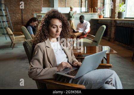 Jeune femme d'affaires utilisant un ordinateur portable tout en étant assise dans un fauteuil au bureau Banque D'Images