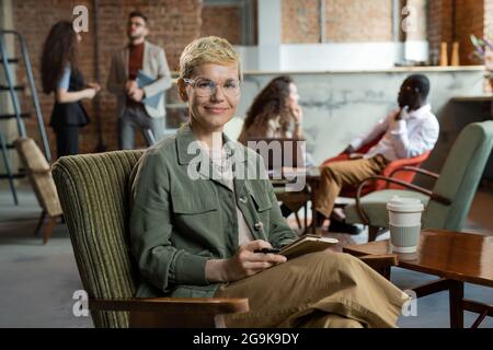 Jeune femme d'affaires souriante aux cheveux blonds courts, assise dans un fauteuil Banque D'Images