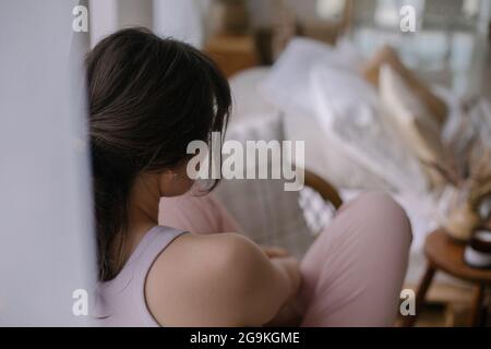 Vue depuis l'arrière de la femme calme et fatiguée assise sur un canapé dans le salon à la maison. Détente à la maison Banque D'Images