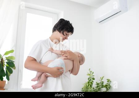 Mère debout ramasse bébé près de l'air conditionné Banque D'Images