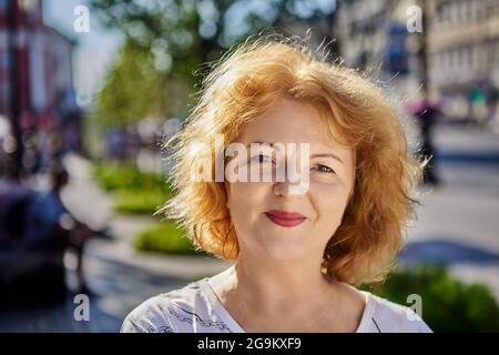 Belle femme d'âge moyen avec des cheveux rouges marche à l'extérieur. Banque D'Images