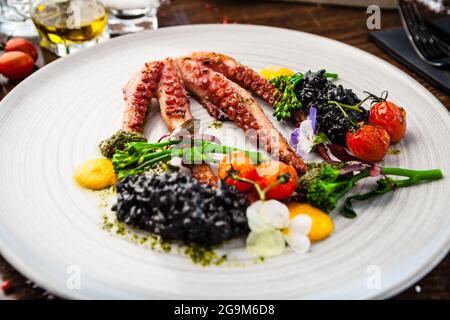 Poulpe avec risotto noir. Crème de carottes, mini-brocoli, pesto de basilic. Une délicieuse cuisine traditionnelle saine est servie pour le déjeuner dans une cuisine gastronomique moderne Banque D'Images