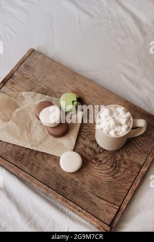 café avec guimauves et macarons sur un plateau en bois, dans le lit. Cadre esthétique. Desserts au lit. Chocolat chaud avec guimauves. Banque D'Images