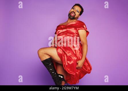 Homme gay portant des vêtements pour femmes dansant et se présentant en studio. Homme androgyne portant une robe rouge brillante. Banque D'Images