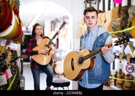 Des adolescents heureux de sexe féminin et masculin choisissent des guitares acoustiques dans un magasin de guitares Banque D'Images
