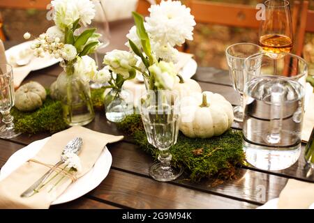 Gros plan de table de style rustique, dîner romantique, couverts, fleurs et petits citrouilles décoratives blanches sur table en bois, arrangeurs Banque D'Images