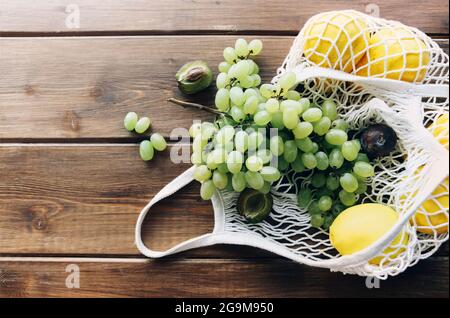 Vue de dessus de maille d'épicerie tricotée avec fruits biologiques plat sur fond de table en bois, des grappes de raisins et des citrons tombent du sac. F Banque D'Images