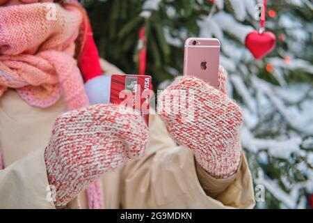 Une femme tient un iphone et une carte bancaire dans ses mains à un arbre de Noël en nature d'hiver à la Saint-Sylvestre - Moscou, Russie, 07 décembre 2020 Banque D'Images