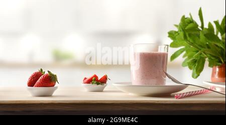 Verre rempli de smoothie fraise sur banc en bois plein de fruits dans la cuisine. Vue avant. Banque D'Images