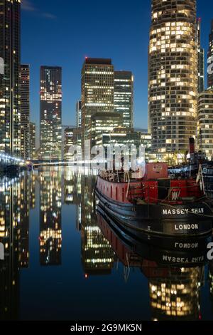 Un bateau-pompier historique, Massey Shaw, amarré sur des eaux calmes la nuit avec les gratte-ciel illuminés de Canary Wharf reflétés derrière lui. Banque D'Images