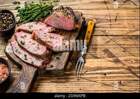Tranches rares de rôti de boeuf sirloin à trois pointes steak bbq sur une planche à découper en bois. fond en bois. Vue de dessus. Copier l'espace Banque D'Images