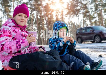 Deux adorables mignons petits frères et sœurs caucasiens enfants garçon fille aiment boire du thé chaud ou du chocolat dans une tasse de papier et manger sur lumineux Banque D'Images