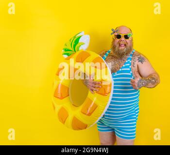 FAT Happy man avec perruque dans la tête est prêt à nager avec un donut sauvetage Banque D'Images
