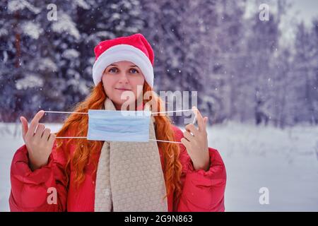 Femme souriante enlève le masque médical, forêt d'hiver avec des arbres dans la neige Banque D'Images