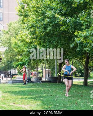 ASHEVILLE, NC, USA-22 JUILLET 2021: Un homme et une femme se produit à Pack Square, elle avec un hula hoop, il jongle balles. Végétation luxuriante en arrière-plan. Banque D'Images