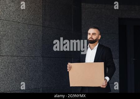 Homme d'affaires montrant un panneau de carton vide, protestant seul contre le confinement dans la rue, espace libre Banque D'Images