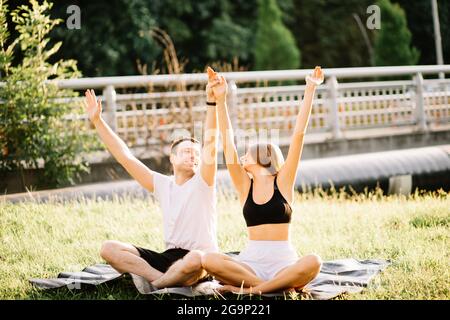 Jeune couple homme et femme faisant du sport, yoga sur la pelouse de la ville, soirée d'été Banque D'Images