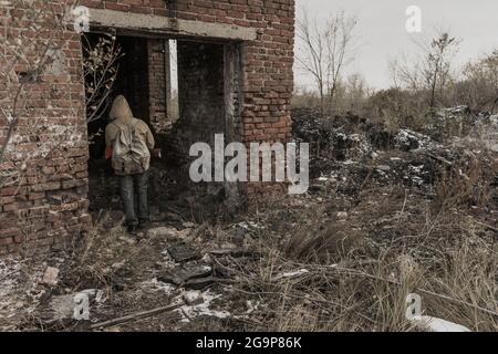 garçon errant. garçon avec une arme. garçon va dans un bâtiment abandonné. garçon se tient devant un bâtiment. Après l'apocalypse. Homme voyageant à pied dans un post- Banque D'Images