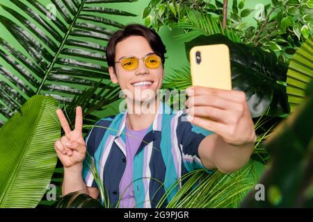 Photo de brunet cool millennium gars dans la jungle ne selfie porter des lunettes chemise isolée sur fond vert couleur Banque D'Images