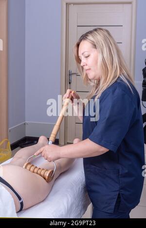 Madero-thérapie massage anti-cellulite, massage de drainage lymphatique - UNE jolie masseuse caucasienne massage le dos du patient de la cuisse avec un bois Banque D'Images