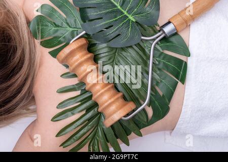 Madero thérapie, massage relaxant - masseur à roulettes allongé sur des feuilles vertes sur le dos d'une femme, gros plan, vue du dessus. Concept de soins du corps Banque D'Images