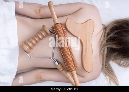 Madero thérapie, massage relaxant anti-cellulite - outils de massage en bois à pointes roulantes, broche roulante, plaque couchée sur le dos d'une femme, vue de dessus, gros plan Banque D'Images