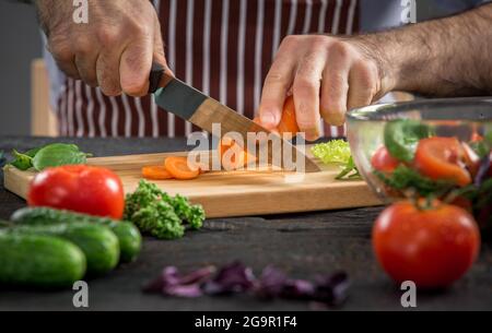 Close up on coupe les mains des hommes, faisant de carottes salade. Couper les légumes en chef. Mode de vie sain, alimentation nourriture Banque D'Images