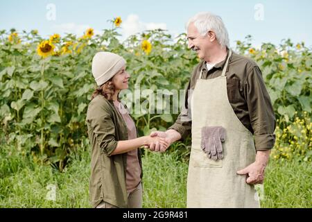 Joyeux agriculteur de sexe masculin et sa collègue de sexe féminin bouteille d'huile de tournesol contre laquelle se trouve la caméra champ vert Banque D'Images