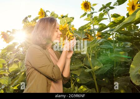 Blonde jeune femme dans une élégante robe blanche tenant une bouteille de huile de tournesol en se tenant contre les feuilles vertes devant caméra sur le terrain Banque D'Images