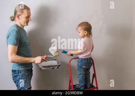 Personne tenant le rouleau de peinture sur le mur gris. Père avec enfant peint mur dans la nouvelle maison, faisant la décoration et re-design de la chambre, ayant l'amusement pendant Banque D'Images