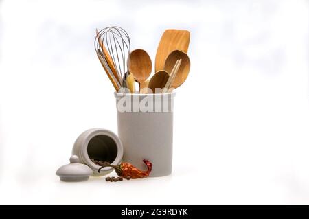 Ustensiles en bois pour cuisiner dans un verre blanc et du piment rouge. Cuillères de cuisine, pelles, fourchettes isolées sur fond blanc. Style scandinave dans le Banque D'Images