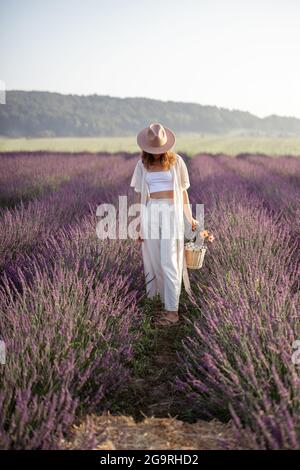 Jeune femme en chapeau restant sur le champ de lavande avec bouquet de fleurs et profiter de la beauté de la nature. Calme et esprit concept. Copier l'espace Banque D'Images