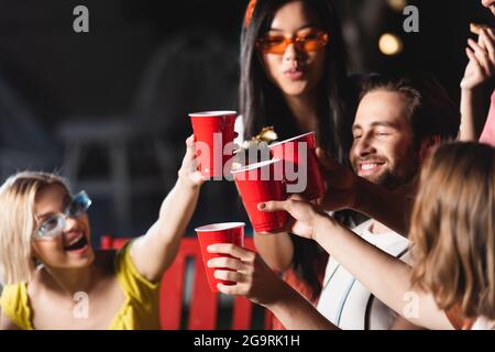 Tasses en plastique dans les mains d'amis interraciaux en grillage sur fond flou Banque D'Images