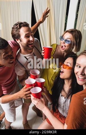 Des amis interraciaux souriants et excités se savourent avec un verre dans le patio pendant la fête Banque D'Images