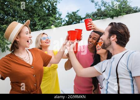 joyeux amis multiculturels en dégustant des tasses en plastique pendant la fête estivale Banque D'Images