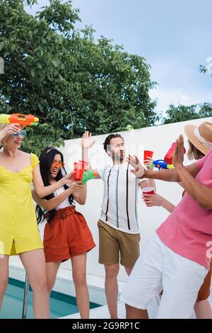 heureux amis interraciaux s'amuser avec des pistolets à eau pendant la fête d'été Banque D'Images