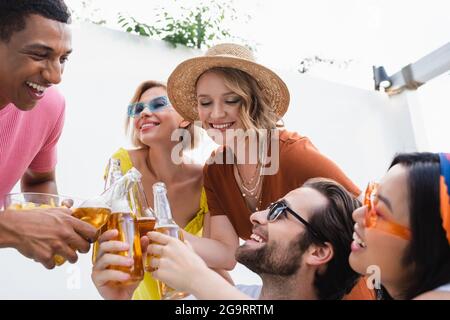 des amis multiculturels heureux se sont servis de bouteilles de bière pendant la fête d'été en plein air Banque D'Images