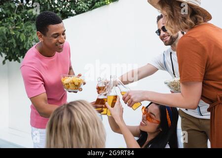 des amis multiethniques excités se sont embués de bouteilles de bière pendant la fête d'été Banque D'Images