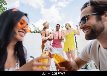 l'homme et la femme interraciaux flous clinquant des bouteilles de bière près des amis heureux Banque D'Images
