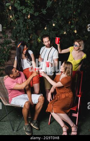 Amis interraciaux dans des lunettes de soleil tenant des tasses en plastique à l'extérieur Banque D'Images