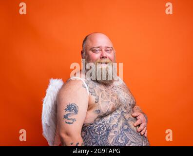 Gros homme heureux avec la barbe, tatouages et ailes agit comme un ange Banque D'Images