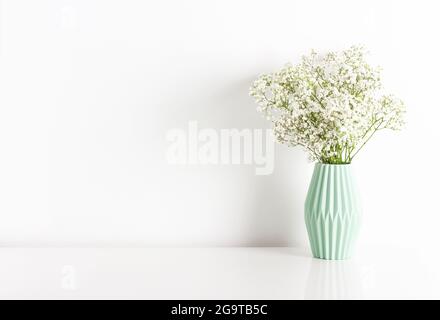 Fleur de gitsophila blanche dans un vase en céramique vert clair sur fond de mur blanc. Décoration intérieure concept. Placer pour le texte. Banque D'Images