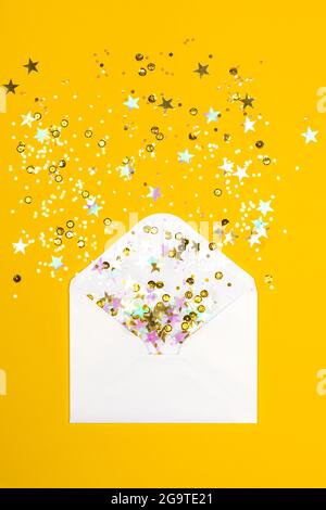 Confettis mousseux déversant de l'enveloppe blanche sur fond jaune. Vue de dessus. Pose à plat. Concept de vacances, de félicitations ou de bonnes nouvelles. Banque D'Images