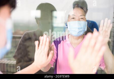 La femme âgée en masque médical communique avec sa fille par la fenêtre. Personnes âgées en quarantaine, isolées. Coronavirus pandémique covid-19 Banque D'Images