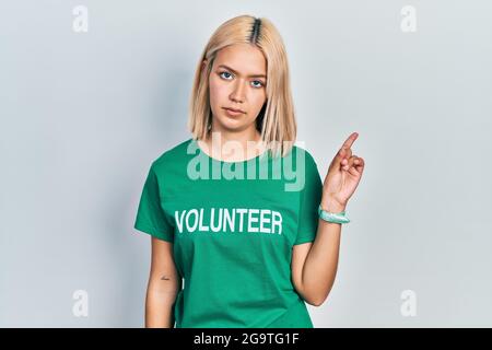 Belle femme blonde portant le t-shirt volontaire pointant avec le doigt de la main sur le côté montrant la publicité, sérieux et calme visage Banque D'Images