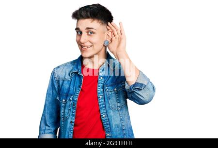 Jeune garçon caucasien avec des oreilles dilatation portant une veste en denim décontractée souriant de la main sur l'oreille écoutant une audition de rumeurs ou de potins. La surdité concresse Banque D'Images