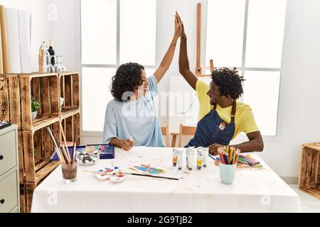 Couple d'artistes afro-américains souriant cinq heureux élevé assis sur la table au studio d'art. Banque D'Images